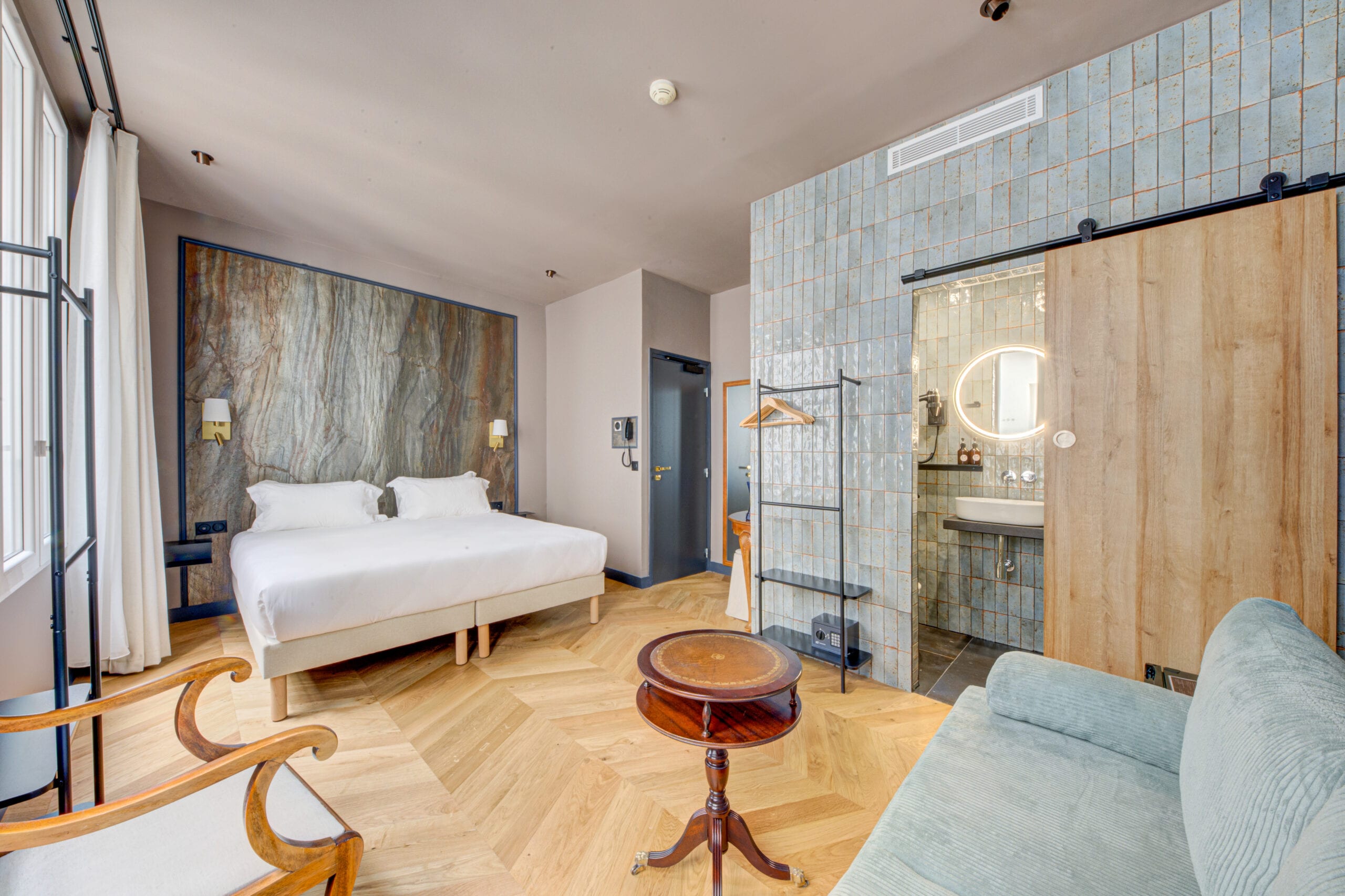 Suite de l’Hôtel Maât Batignolles : tête de lit en marbre, appliques en laiton, parquet à chevrons